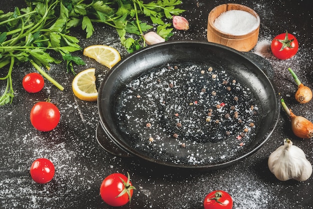 Ingredienti e spezie per cucinare la cena: pomodori, verdure (prezzemolo), sale, pepe, cipolle, scalogno, aglio. Con una padella, su un tavolo di cemento nero, copia spazio