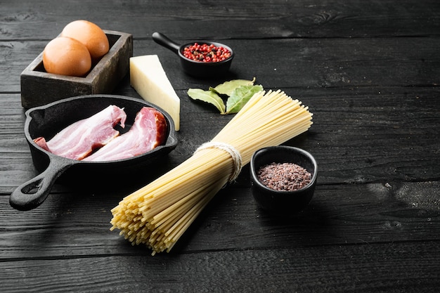 Ingredienti grezzi freschi per l'insieme della carbonara della pasta italiana tradizionale, su fondo di legno nero, con lo spazio della copia per testo