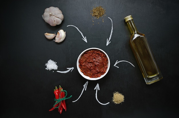 Ingredienti Harissa per la cottura di peperoncino piccante, sale marino grosso, aglio, cumino zira, olio d'oliva, coriandolo macinato su un tavolo di ardesia scuro. adjika, muhammara.