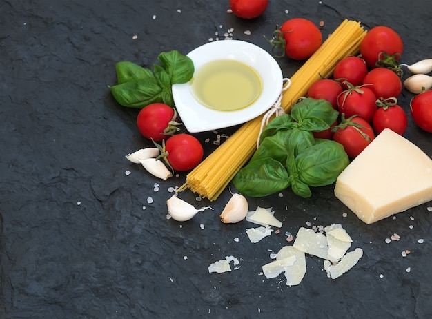 Ingredienti per cucinare la pasta. Spaghetti, olio d'oliva, aglio, parmigiano, pomodori e basilico fresco