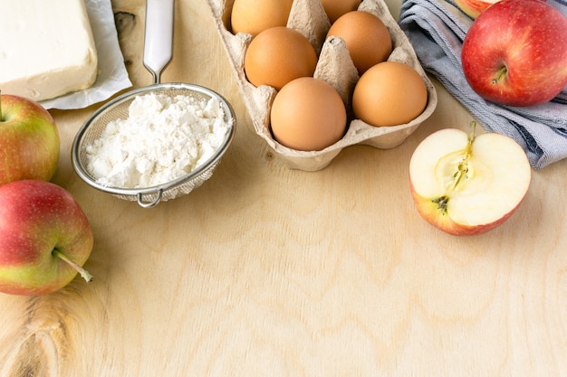 Ingredienti per cucinare la torta di mele. Uova, farina e burro su fondo di legno, copyspace