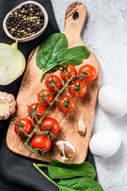 Ingredienti per cucinare Shakshuka. Uova, cipolle, aglio, pomodori, peperoni, spinaci. Sfondo grigio. Vista dall'alto.