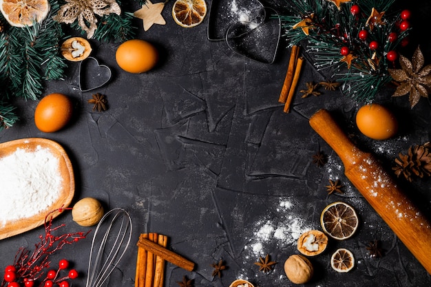 Ingredienti per cuocere i biscotti di Natale su uno sfondo nero, vista dall'alto, copia dello spazio.