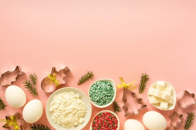 Ingredienti per cuocere i biscotti di Natale. Uova, farina, zucchero e granelli dolci su uno sfondo rosa con spazio di copia.