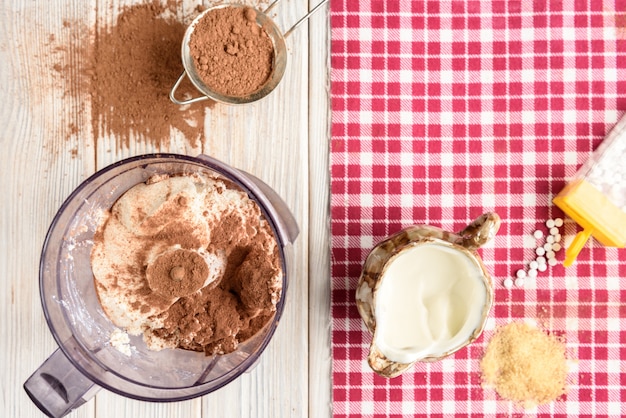 Ingredienti per il dessert soufflé di ricotta fatta in casa con cacao sulla tavola di legno bianca.