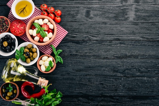 Ingredienti per l'insalata caprese italiana Mozzarella pomodorini basilico foglie olive olio pepe Su fondo di legno nero Spazio libero per il testo