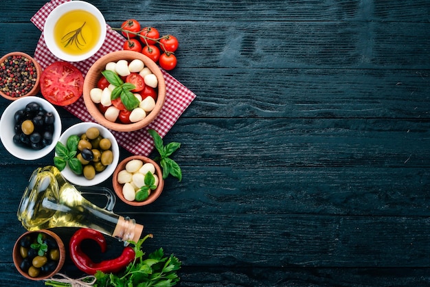 Ingredienti per l'insalata caprese italiana Mozzarella pomodorini basilico foglie olive olio pepe Su fondo di legno nero Spazio libero per il testo