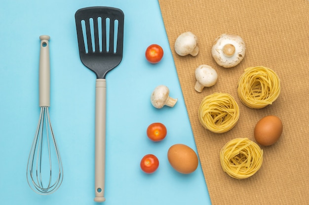 Ingredienti per la cottura della pasta con funghi e pomodori e utensili da cucina.