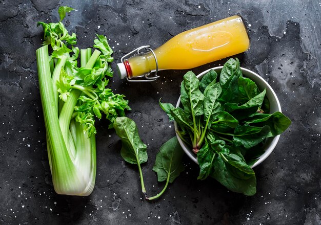 Ingredienti per la dieta detox frullati verdi sedano fresco spinaci succo d'arancia naturale su sfondo scuro vista dall'alto