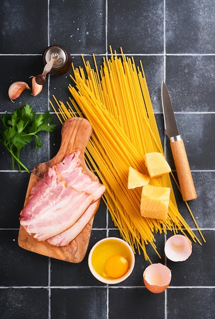 Ingredienti per la pasta alla carbonara Pasta tradizionale italiana alla carbonara Ingredienti pancetta spaghetti parmigiano e tuorlo d'uovo aglio Sfondo nero vecchio tavolo piastrella Vista dall'alto Spazio di copia