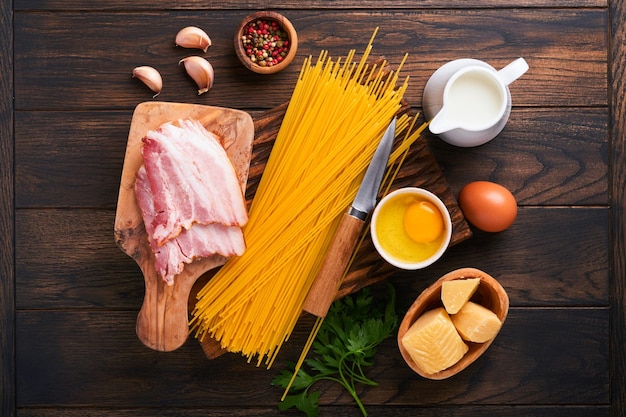 Ingredienti per la pasta alla carbonara Pasta tradizionale italiana alla carbonara Ingredienti pancetta spaghetti parmigiano e tuorlo d'uovo aglio Sfondo vecchio tavolo in legno scuro Vista dall'alto Spazio di copia