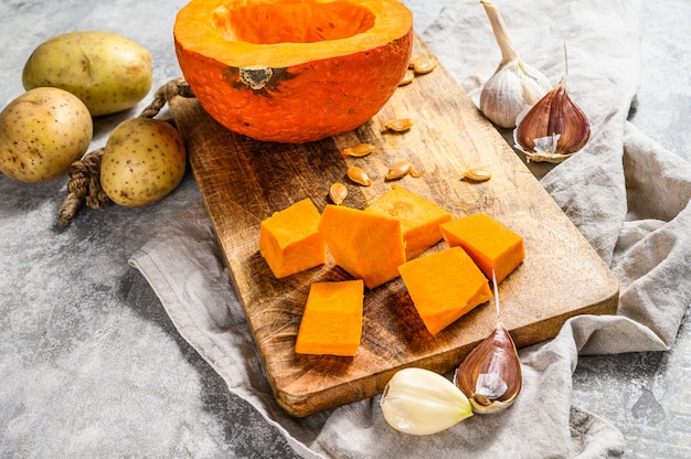 Ingredienti per la zuppa di zucca. Muro grigio. Zucca tagliata sul tagliere rustico. Cibo gustoso e salutare. Cibo vegano