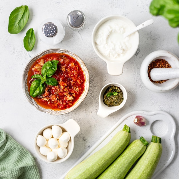 Ingredienti per rotoli di zucchine con formaggio a crema e salsa di pomodoro su uno sfondo bianco