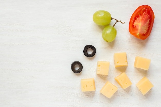 Ingredienti per snack, formaggio con olive e pomodoro su un tavolo bianco