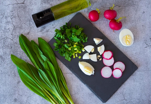 Ingredienti per un'insalata con aglio orsino su fondo di cemento un mazzetto di uovo di ciliegia olio di ravanello