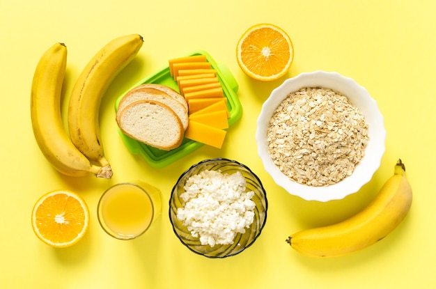 Ingredienti per una sana colazione. Farina d'avena, latticini e frutta sulla superficie gialla, vista dall'alto.