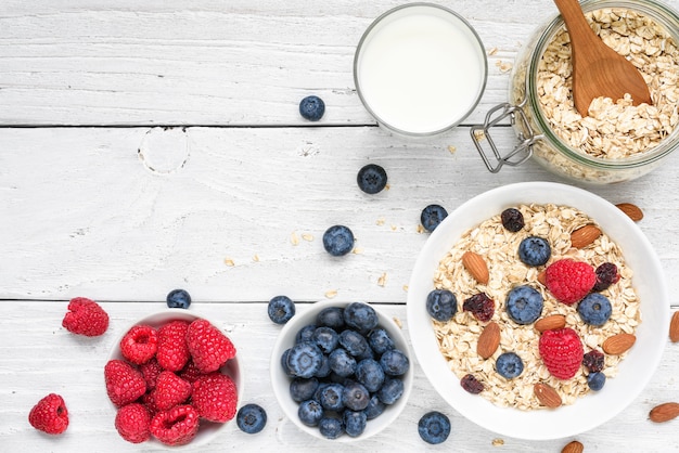 Ingredienti salutari per la colazione. avena fatta in casa con lamponi e mirtilli, latte e noci sul tavolo di legno bianco