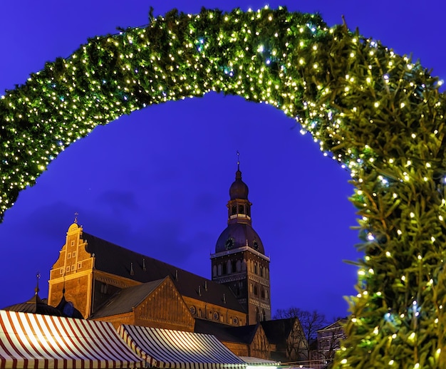 Ingresso al mercatino di Natale e alla Cattedrale di Riga sullo sfondo nella piazza del Duomo nella vecchia Riga, Lettonia. La Cattedrale di Riga o Duomo fu costruita nel 1211 dal vescovo livoniano Alberto di Riga.