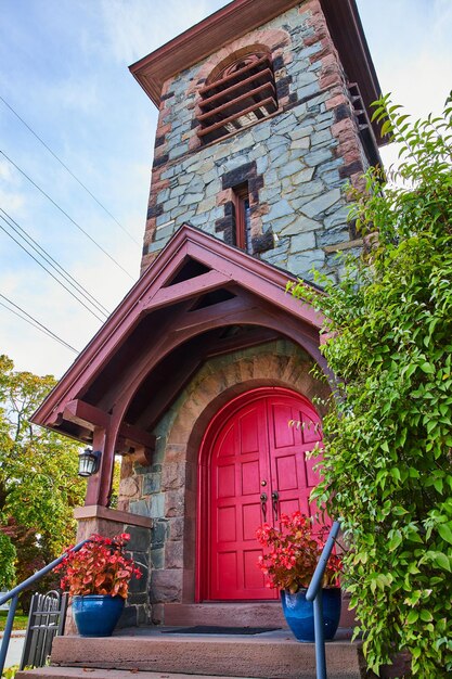 Ingresso anteriore alla chiesa in pietra con enormi doppie porte rosse e campanile con vegetazione