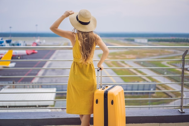 Inizio del suo viaggio Bella giovane donna ltraveler in un vestito giallo e una valigia gialla sta aspettando il suo volo