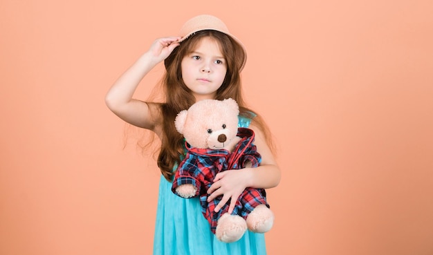 Innamorato del simpatico orsacchiotto Infanzia felice Allegati teneri Capretto bambina abbraccio con attenzione peluche orsacchiotto sfondo beige Il più carino di sempre Piccola ragazza cappello di paglia tenere orsacchiotto peluche