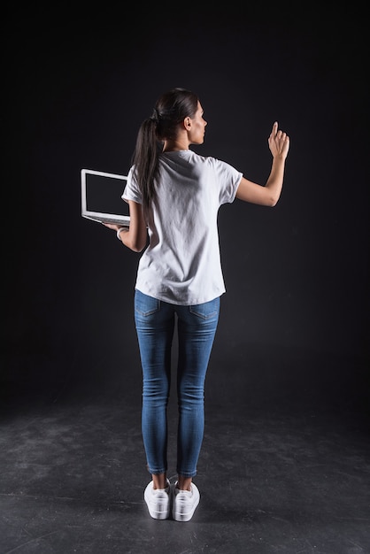 Innovazioni moderne. Piacevole bella donna attraente in piedi e tenendo il suo laptop mentre si utilizza la tecnologia progressiva