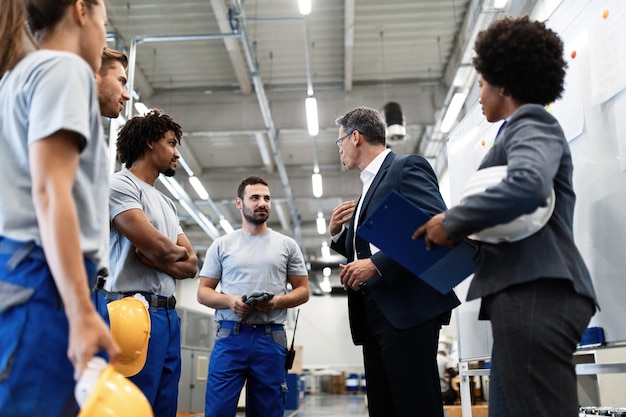 Inquadratura dal basso dell'uomo d'affari che parla con un team di lavoratori manuali mentre si riunisce il personale in uno stabilimento industriale