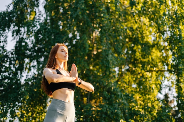 Inquadratura dal basso di donna rossa meditativa che pratica yoga esibendosi facendo saluto a mano namaste