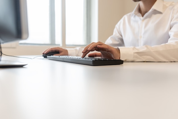 Inquadratura dal basso di un uomo d'affari in camicia bianca che digita sulla tastiera di un computer.