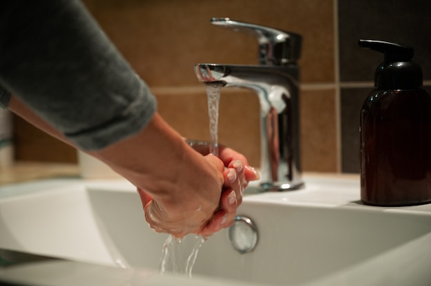 Inquadratura dal basso di una donna che si lava le mani nel bagno di casa usando sapone e acqua di rubinetto.