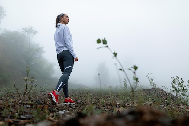 Inquadratura dal basso di una sportiva che parla di una passeggiata nella natura durante il tempo freddo e nebbioso Copia spazio