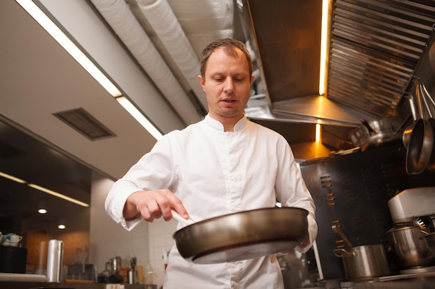 Inquadratura dal basso di uno chef del ristorante che cucina in cucina, usando una padella