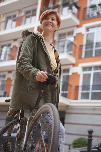 Inquadratura dal basso verticale di una giovane donna allegra che si appoggia sulla sua bicicletta