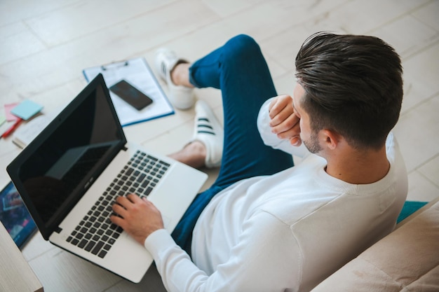 Inquadratura dall'alto di un uomo che naviga in Internet sul computer seduto sul pavimento a casa tecnologia online di...