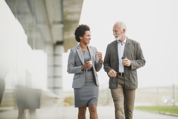 Inquadratura di due uomini d'affari multietnici di successo che si divertono mentre camminano durante una pausa caffè davanti all'edificio degli uffici.