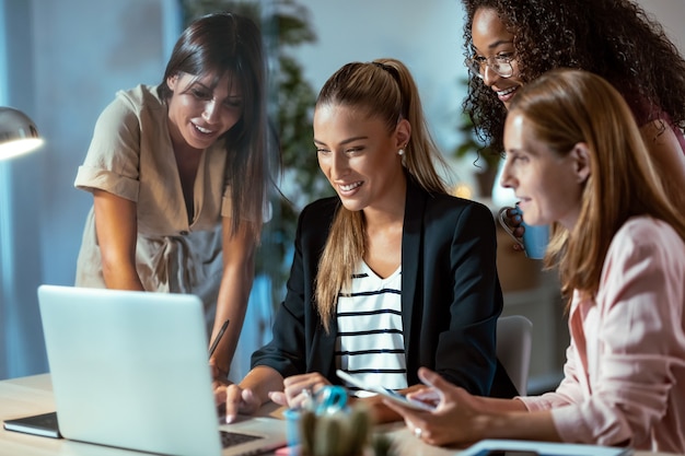 Inquadratura di quattro donne d'affari intelligenti che parlano e rivedono l'ultimo lavoro svolto al computer in un'area di lavoro comune.