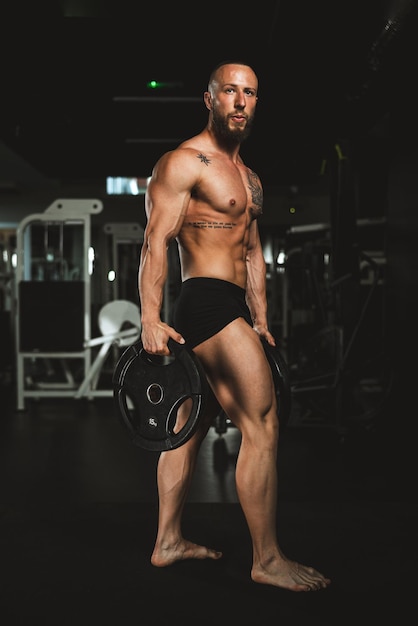 Inquadratura di un bodybuilder muscoloso che mostra i suoi muscoli perfetti dopo l'allenamento con il piatto di peso in palestra.