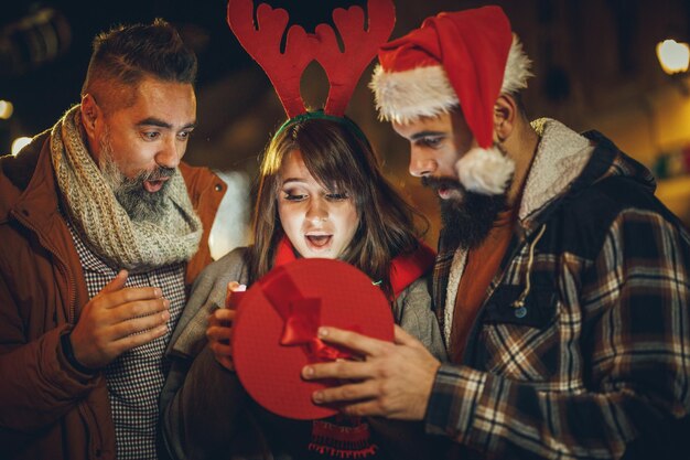 Inquadratura di un gruppo di giovani amici allegri che sembrano eccitati dopo aver ricevuto un regalo di Natale e divertirsi durante una serata fuori.