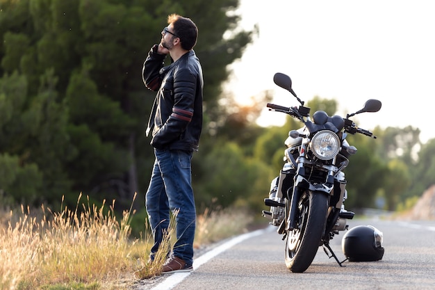Inquadratura di un motociclista che parla al telefono con l'assicurazione della sua moto dopo aver subito un guasto sulla strada.