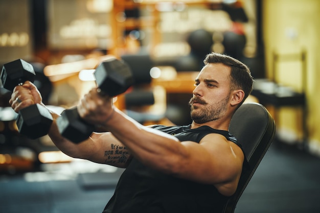 Inquadratura di un ragazzo muscoloso in abbigliamento sportivo che si allena con i manubri nella palestra di cross training.