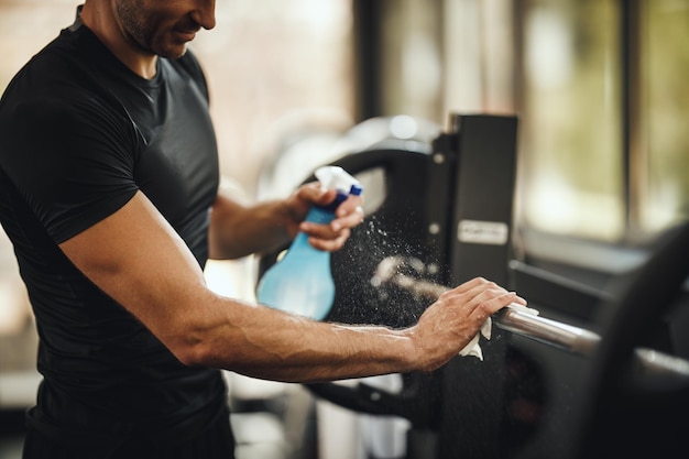 Inquadratura di un uomo muscoloso e irriconoscibile che pulisce l'attrezzatura da palestra prima dell'allenamento durante la pandemia di Covid-19.