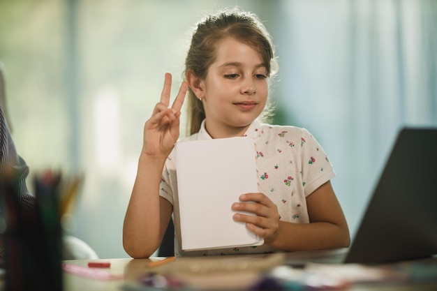 Inquadratura di una bambina diligente che usa il laptop per fare una lezione online a casa durante la pandemia di COVID-19.