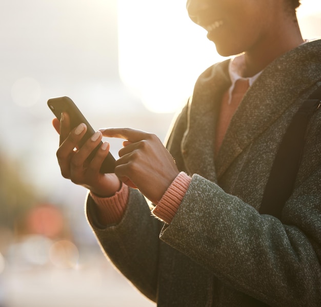 Inquadratura di una donna d'affari che usa un ombrello e uno smartphone mentre fa una passeggiata sotto la pioggia su uno sfondo urbano