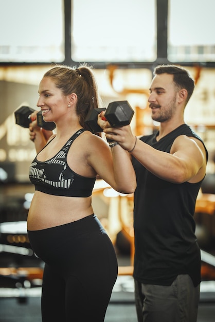 Inquadratura di una donna incinta che si allena con un manubrio sotto il controllo del personal trainer in palestra.