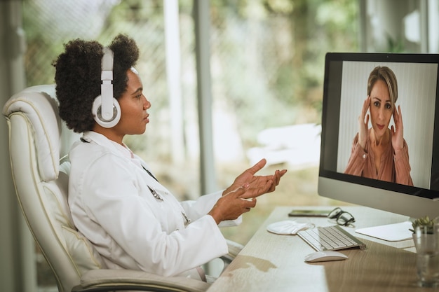 Inquadratura di una dottoressa africana che fa una videochiamata con un paziente al computer nella sua stanza di consultazione durante la pandemia di COVID-19.