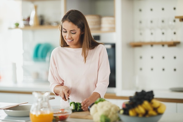 Inquadratura di una giovane donna che taglia le verdure e prepara un pasto sano nella sua cucina.