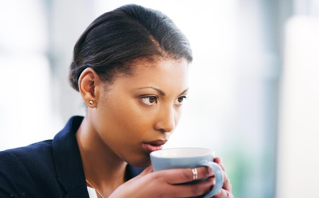 Inquadratura di una giovane donna d'affari che si concentra mentre utilizza un computer e beve un caffè in un ufficio moderno