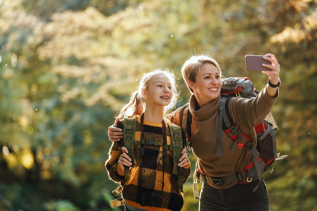 Inquadratura di una ragazza adolescente e sua madre che si fanno un selfie durante una passeggiata insieme attraverso la foresta in autunno.