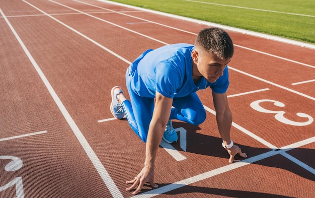 Inquadratura orizzontale del giovane atleta maschio in posizione di partenza pronto per iniziare una gara Velocista uomo pronto per l'esercizio sportivo in pista nello stadio Stile di vita sportivo e concetto di persone