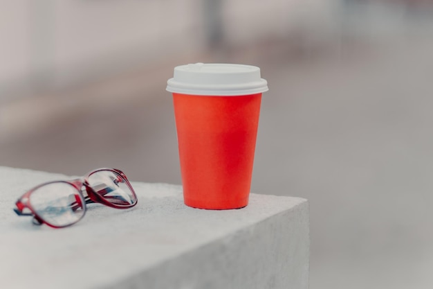 Inquadratura orizzontale di caffè rosso da asporto e occhiali ottici Caffè aromatico da bere Concetto di bevanda Tazza di carta di bevanda calda